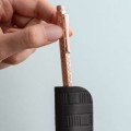 Dłoń trzymająca długopis Caran d’Ache Ecridor Damier Rose Gold, wysuwająca go ze skórzanego etui.