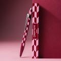 Artystyczne ujęcie długopisu Caran d’Ache 849 Mosaic Garnet Red opartego o ciemnoczerwoną ściankę, eksponujące klips i wzór geometryczny.