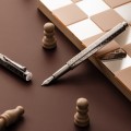 Artystyczne ujęcie pióra wiecznego Caran d'Ache Ecridor Damier na szachownicy obok drewnianych figur szachowych podkreślające wzór giloszowania.