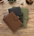 Trzy organizery Filofax Camden Personal w kolorach brazowym czarnym i oliwkowym ukladane warstwowo na drewnianym blacie
