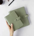 Zamkniety-zielony-organizer-Filofax-Malden-Personal-Vetiver-trzymany-w-dloni-nad-wiekszym-planerem