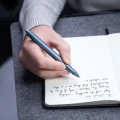 Mężczyzna piszący niebieskim piórem kulkowym Novium Hoverpen Future Deep Blue w otwartym notesie