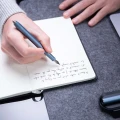 Mężczyzna piszący niebieskim piórem wiecznym Novium Hoverpen Future Deep Blue w notesie na filcowej macie